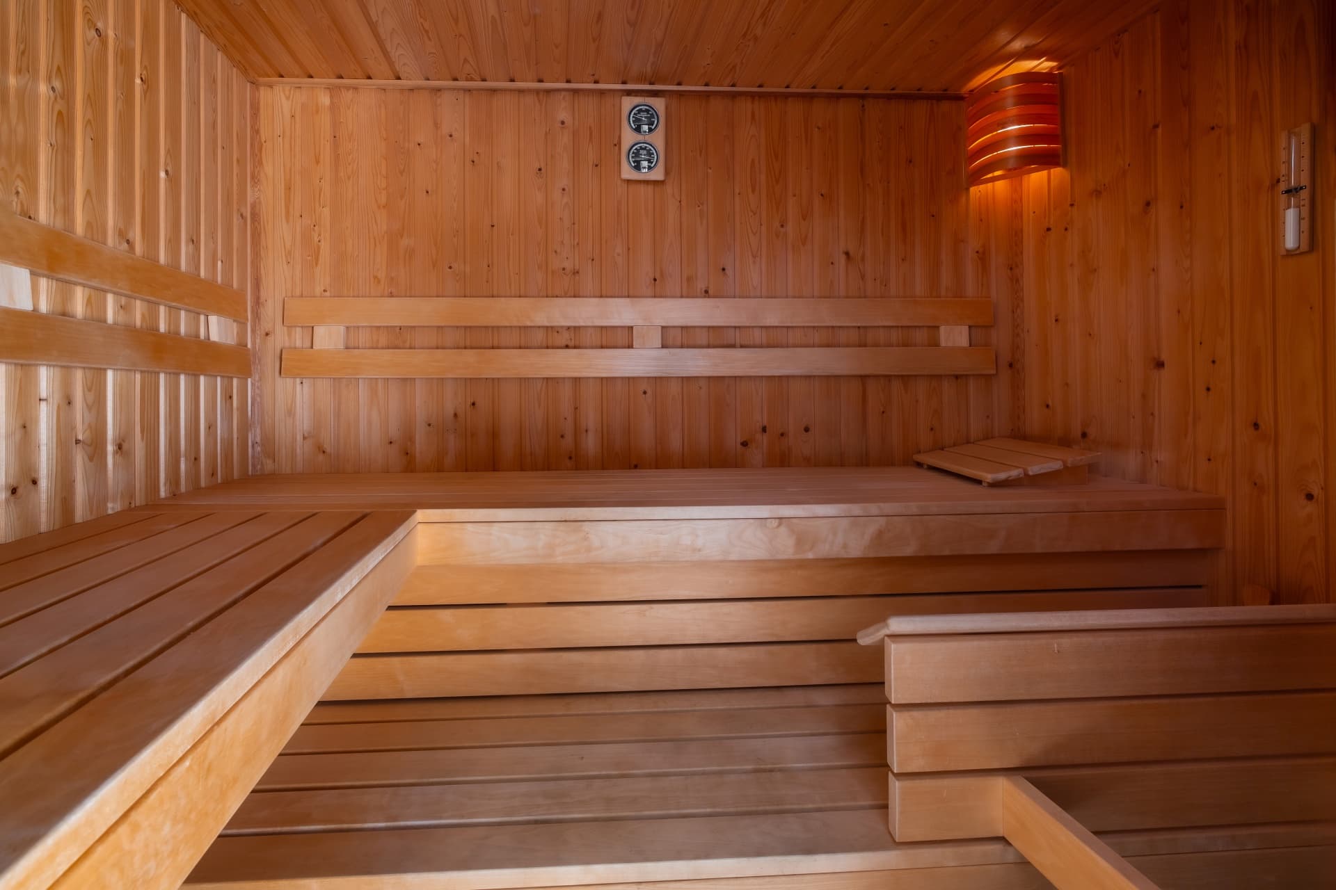 Traditional wooden sauna interior with tiered benches, wall-mounted thermometer, and warm ambient corner lighting.