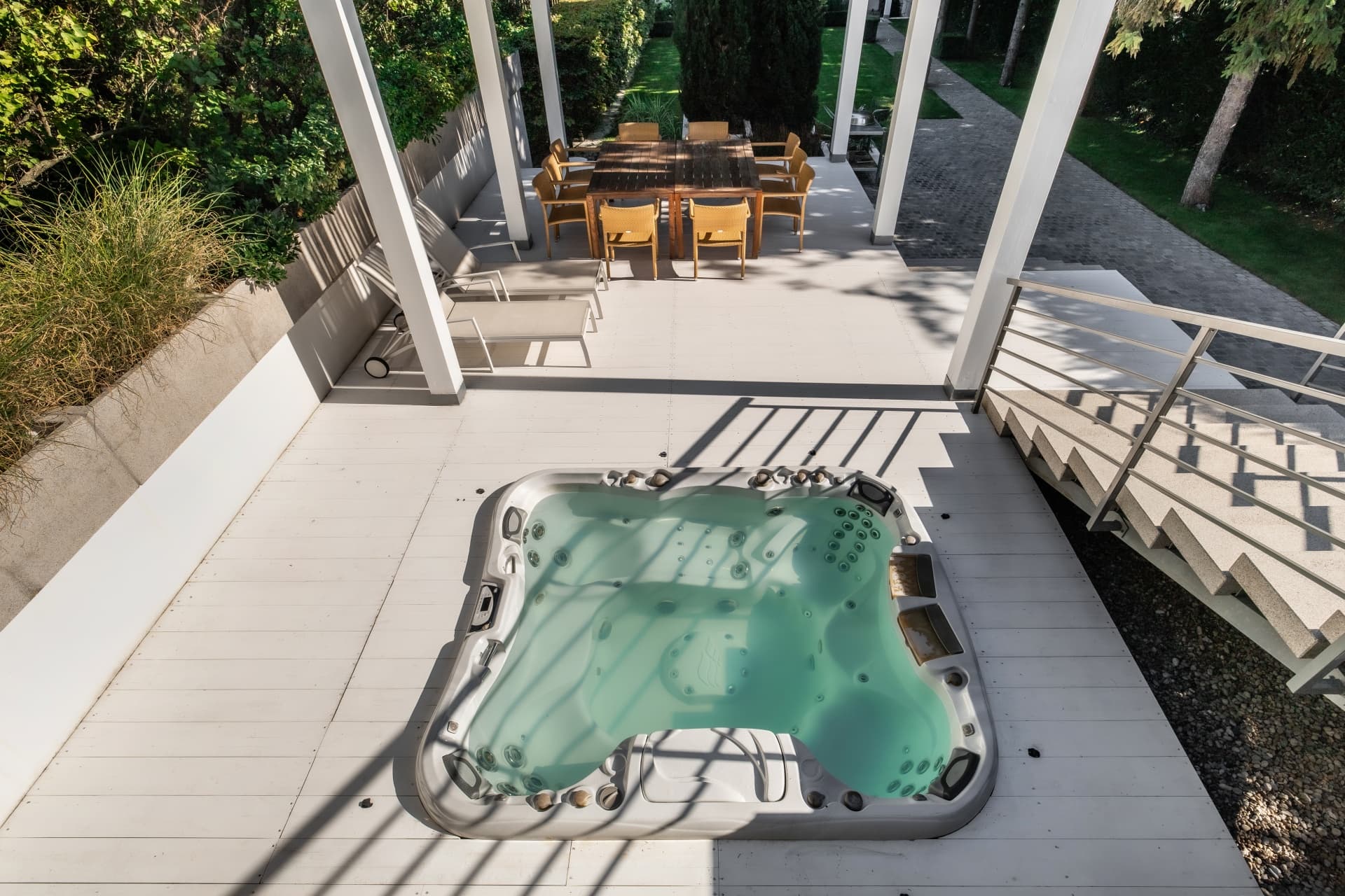 Modern white deck with a built-in hot tub, dining area, and lush green garden.